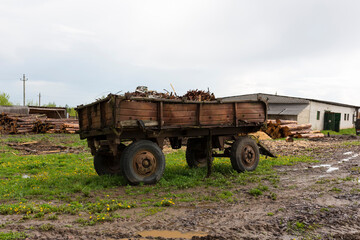 Old abandoned rusty tractor trailer. Stands on a green lawn in a muddy puddle.