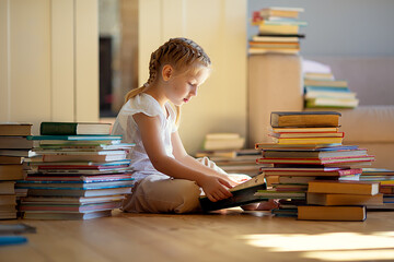 A little cute girl in a yellow dress reading a book sitting on the floor