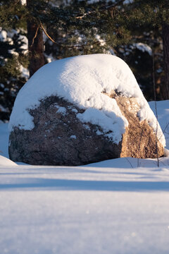 A rural scene of sunny winter day with a block of granite covered in snow.
