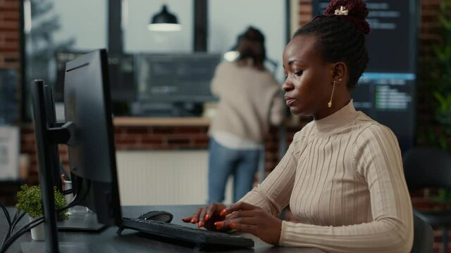 African american software engineer working focused looking at computer screen while typing in it startup office. Database programer writing code with algorithms compiling on screens in background.