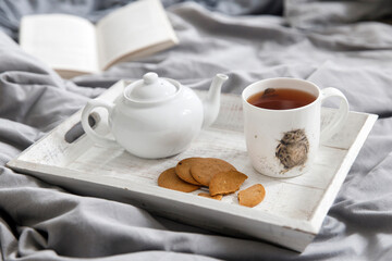 Fototapeta na wymiar interior and home cosiness concept. Top view. A cup of tea, a teapot with herbal tea, sugar bowl on a wooden tray on the bed