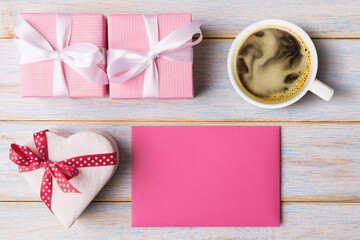 Gift boxes, cup of coffee and blank pink card on light wooden background