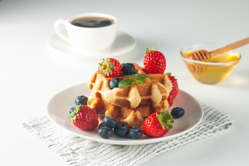 Fresh homemade food of berry Belgian waffles with honey, chocolate, strawberry, blueberry, maple syrup and cream. Healthy dessert breakfast concept with juice