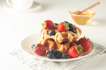 Fresh homemade food of berry Belgian waffles with honey, chocolate, strawberry, blueberry, maple syrup and cream. Healthy dessert breakfast concept with juice