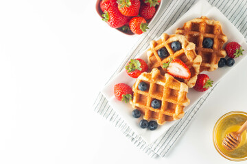 Fresh homemade food of berry Belgian waffles with honey, chocolate, strawberry, blueberry, maple syrup and cream. Healthy dessert breakfast concept with juice