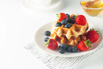 Fresh homemade food of berry Belgian waffles with honey, chocolate, strawberry, blueberry, maple syrup and cream. Healthy dessert breakfast concept with juice