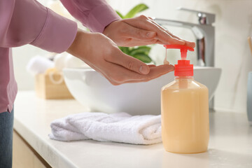 Woman using liquid soap dispenser in bathroom, closeup - obrazy, fototapety, plakaty