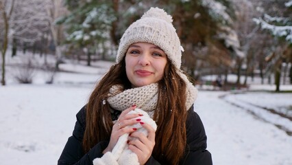 Young beautiful caucasian woman goulash in snowy winter park close up in slow motion. Happy girl with long brown hair enjoys winter and smiles on Christmas Eve and Happy New Year