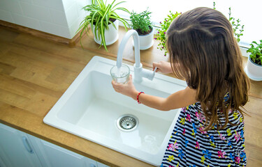 Children picks up a glass of water from the tap. Selective focus.
