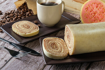 Bolo de rolo slice closeup surrounded by cutlery, guava, cup and coffee beans.