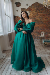 Fototapeta premium A beautiful girl in a green dress smile shows a brick wall dress