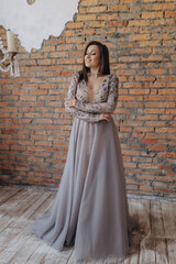 A beautiful girl in a gray dress smile shows a brick wall dress