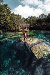 Hombre joven latino parado en una roca dentro de un cenote cristalino