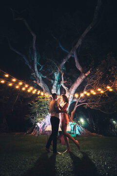 Pareja abrazada mir&aacute;ndose al anochecer frente a un &aacute;rbol en una cita