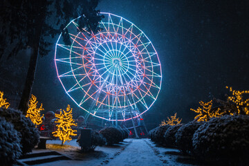 Magic winter park with amusement rides and amazing glowing neon ferris wheel at night with snow - obrazy, fototapety, plakaty
