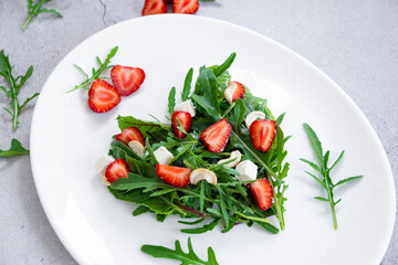 Delicious salad of strawberry with mix of herbs, arugula, spinach leaves, feta cheese and cashew nuts in heart shape on white plate. Vegetarian food and raw food diet.