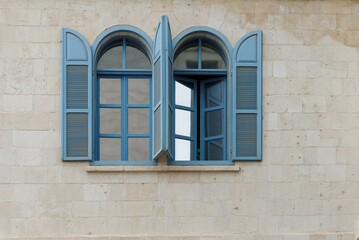 Open windows of the stone building with blue frame and blue wooden blinds