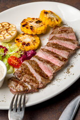 Beef steak sliced with fried corn and begetables on dark brown concrete table macro close up