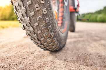 Fototapeta na wymiar Close-up of fat mountain bike tire on dirty road. Fat bike wheel. Summer outdoor activity.