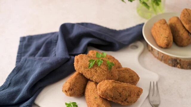 Cod dumplings, or "bolinhos de bacalhau" and parsley leaves on white ceramic dishes in a kitchen counter top.