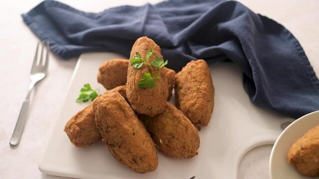Cod dumplings, or "bolinhos de bacalhau" and parsley leaves on white ceramic dishes in a kitchen counter top.