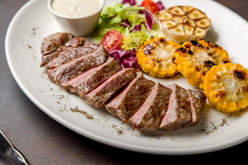 Beef steak sliced with fried corn and begetables on dark brown concrete table macro close up