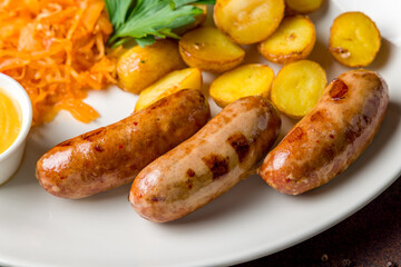 Fried hunter sausage with potatoes, fried cabbage and mustard on white plate on dark brown table macro close up