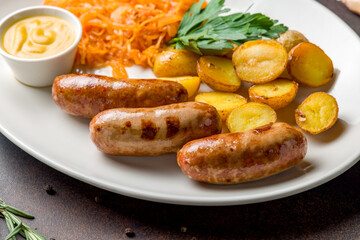 Fried hunter sausage with potatoes, fried cabbage and mustard on white plate on dark brown table macro close up