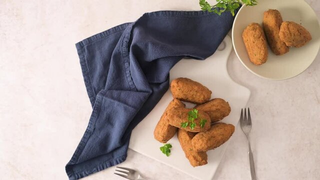 Cod dumplings, or "bolinhos de bacalhau" and parsley leaves on white ceramic dishes in a kitchen counter top.