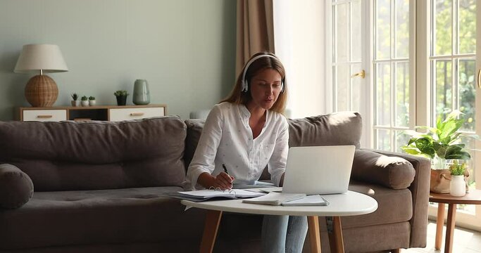 Confident young lady mentor tutor in headset teach pupils students online give remote lesson lecture in virtual classroom video chat app on laptop explain new material make records in class register