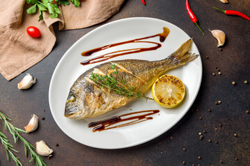 Dorado on grill on a white plate on dark brown concrete table top view