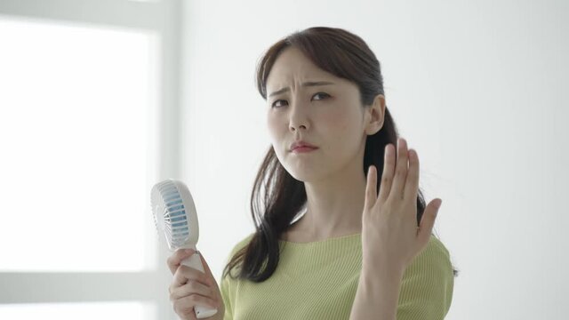 ハンディファンを使う女性　じめじめした梅雨の季節
