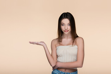 young and pretty woman in crop top pointing with hand isolated on beige