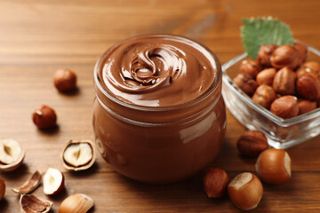 Glass jar with tasty chocolate hazelnut spread and nuts on wooden table