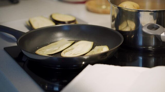 Slices of eggplant frying on pan and steaming, process of cooking organic vegetables on electric stove top in the kitchen. High quality 4k footage
