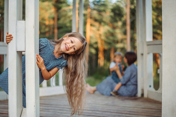 Fototapeta na wymiar A family, a mother with children are relaxing in nature in the forest, in a gazebo. A girl with long hair is playing, smiling, having fun.