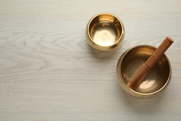 Golden singing bowls and mallet on white wooden table, flat lay. Space for text