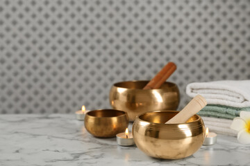 Tibetan singing bowls, mallets, towels and burning candles on white marble table, space for text