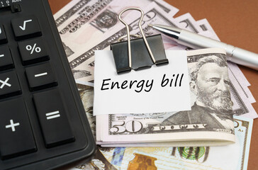 On a brown background lies a calculator and dollars on a clip with an inscription on paper - Energy bill