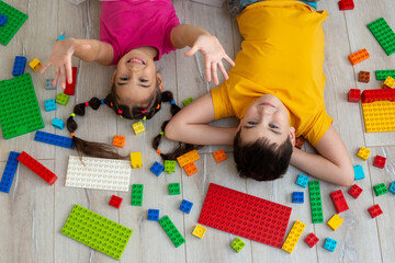Portrait of happy boy and a little girl, lie on the floor with multicolor constructor