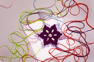 Decorative purple flower and threads of different colors on a gray background. Handmade decoration.