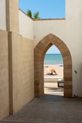 View of the beach through the Portillo del Sur, a gate of the town wall with propped arch , Rota,...