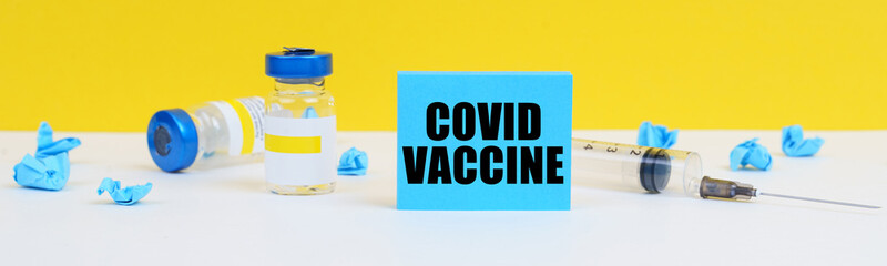 On the table is a syringe, injections and a blue sign with the inscription - COVID VACCINE