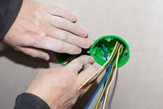 An electrician installs an electrical outlet into the wall. Carrying out electrical wiring in the house