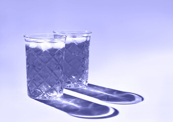 Beautiful crystal glasses cast long shadow from sunlight. Toned in trendy color of year 2022. Minimal creative composition with copy space. Summer drinks concept.