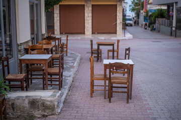 Fototapeta na wymiar Narrow streets of Nea Skioni fishing town in Greece, with cafe-restaurant chairs and tables on street, typical outdoors Greek Tavern on cobblestone street. 