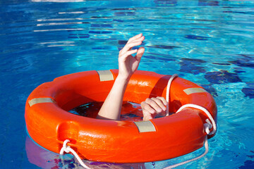 A red lifebuoy on the surface of the water in the pool and the hands of a man grabbing it,...