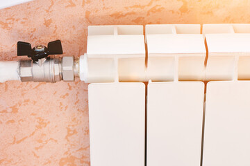 White heating radiator and knob on the wall. Battery and tap. Heating appliances.