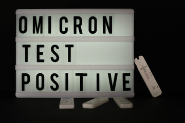 a positive Covid antigen rapid test lies next to a light panel with the inscription Omikron test...