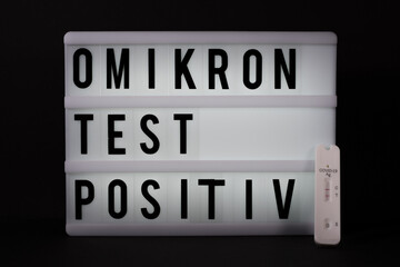 a positive Covid antigen rapid test lies next to a light panel with the inscription Omikron test...
